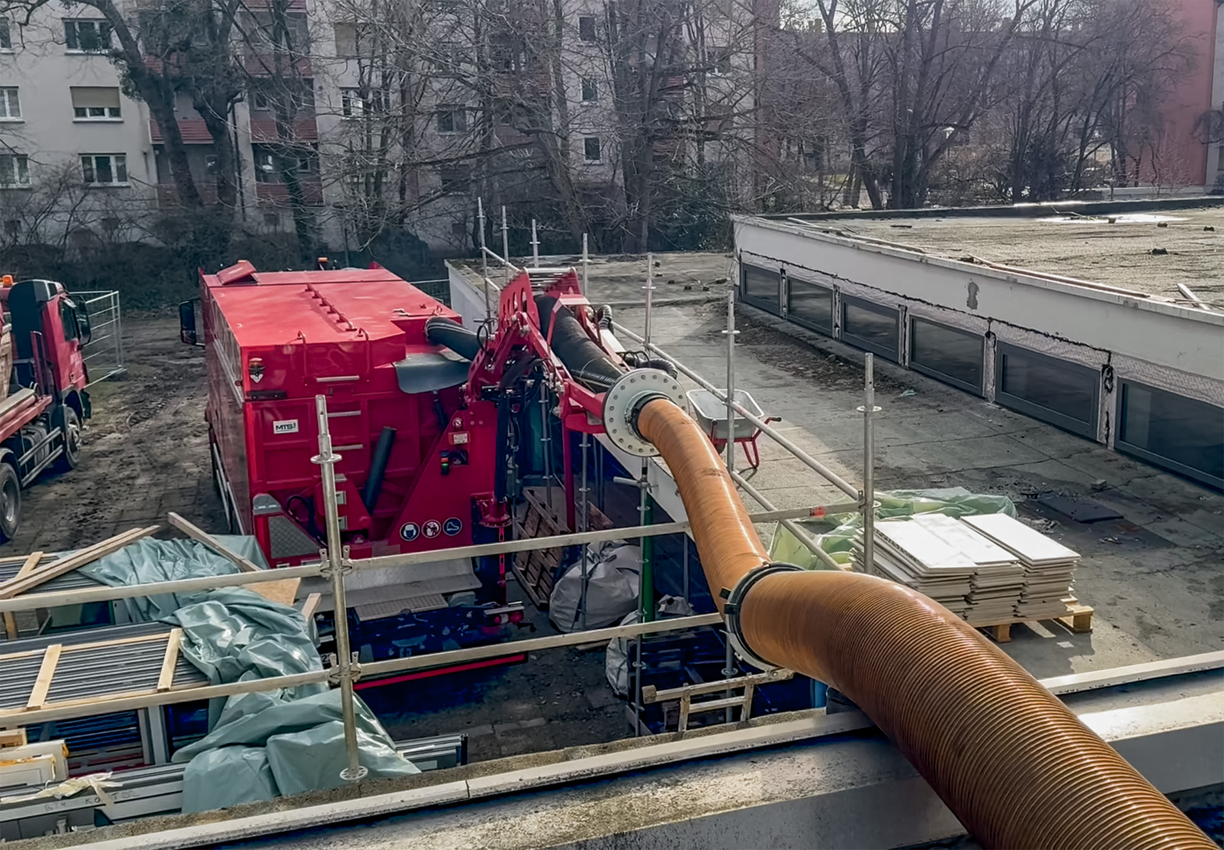 Blick vom Flachdach auf den Saugbagger DINO VARIO von MTS und den MegaArm, mit dem der Saugschlauch leicht das Flachdach erreicht.
